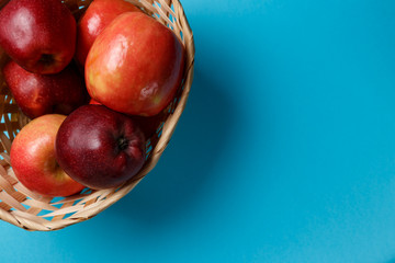 Ripe red apples in a basket on a blue background. Top view