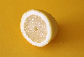 A fresh lemon cut in half on bright, neon yellow background with water drops