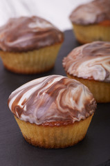 Small cupcakes on a black background close-up macro. Black and white glaze on a sweet dessert. Tiny cakes with zebra decor. Food for guests from the confectioner at the festival.