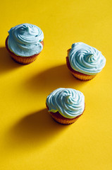 Unusual cupcakes with a beautiful blue cream. Cakes with perfect caps made from protein cream. Whipped cream with blue food color. Treat for children on a yellow-blue background.