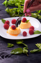 The girl is going to eat delicious panna cotta with caramel sauce small teaspoon. A woman wants to lose weight and eats a dietary dessert. Delicious Italian pudding with fresh mint and raspberries.