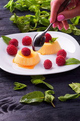 The girl is going to eat delicious panna cotta with caramel sauce small teaspoon. A woman wants to lose weight and eats a dietary dessert. Delicious Italian pudding with fresh mint and raspberries.