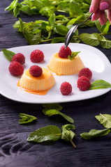 The girl is going to eat delicious panna cotta with caramel sauce small teaspoon. A woman wants to lose weight and eats a dietary dessert. Delicious Italian pudding with fresh mint and raspberries.