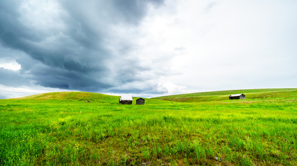 Tin Roofed Barns in the wide open Grass Lands of the Nicola Valley, along Highway 5A between Merritt and Kamloops, British Columbia, Canada, under dark threatening sky