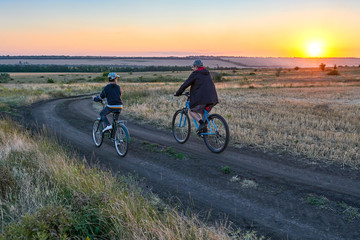 Obraz na płótnie Canvas father and son ride a bike in the country on the field in the evening