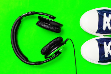 A pair of new stylish sneakers and headphones on a green bright background. Top view. Concept walks to music. Copy space