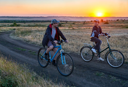 father and son ride a bike in the country on the field in the evening