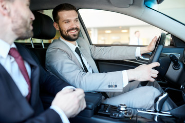 Happy young man sitting behind the wheel of a new car with car dealer near by