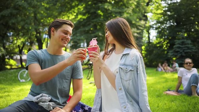 Caucasian young couple wearing casual clothes on picnic. Handsome young man holding blue camera in hand, talking photos with adorable girlfriend. Vacations. Outdoors. Summertime.