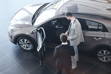 Fototapeta na wymiar Businessman standing near the new car with salesman consulting him in car salon