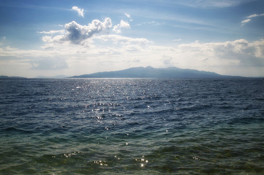 Fototapeta View of the beach and the sea, Corfu island is on the horisont. Blue sea and sky with white clouds. Ionian Sea.
