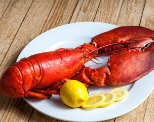 A delicious freshly boiled lobster with lemon on white dish on wood background