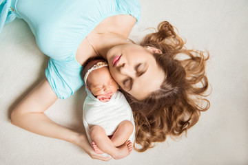 Top view of beautiful young mom and her cute newborn baby sleeping in bed at home