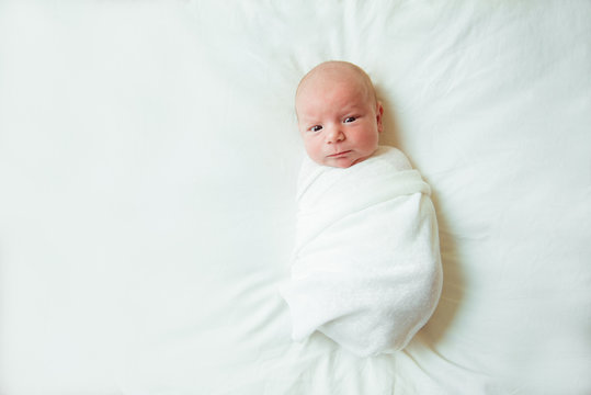 Cute newborn baby lies swaddled in a white blanket. Copy space and top view