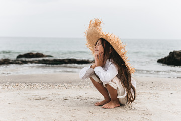 Adorable little girl in straw hat at beach during summer vacation