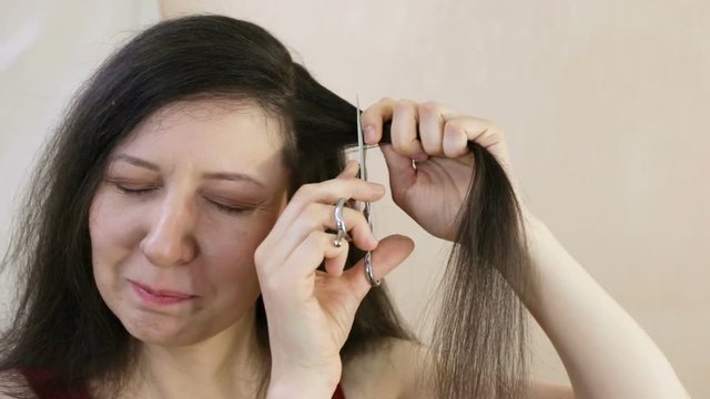 Woman cut her hair too short. The woman feels fear, she takes herself in hand, closes her eyes, laughs nervously and does it. Close-up, indoor, real-time