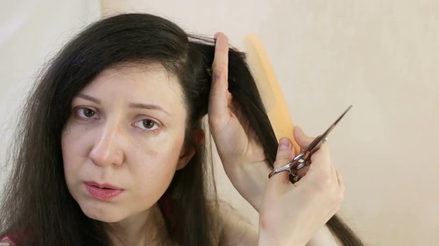 The girl combs a strand of her hair and sighs, she has such symptoms of crisis as fatigue and lack of oxygen. Close-up, indoor, real time