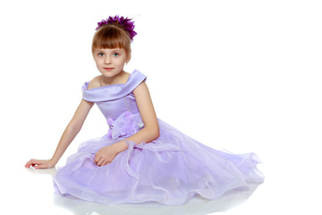 Girl sits on the floor with her hands folded in front of her.