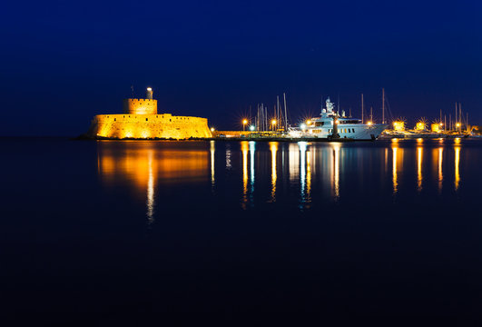 Night photo of ancient fortress and pier in Rhodes city on Rhodes island, Dodecanese, Greece. Stone walls and bright night lights. Famous tourist destination in South Europe