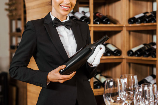 cropped shot of smiling female wine steward holding bottle at wine store