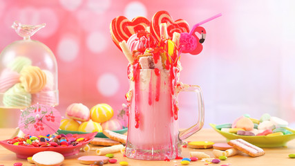 Making modern popular trend strawberry freak shakes milkshakes toppping with lollipops candy and cookies, selective focus.