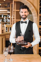 handsome young sommelier holding decanter of red wine at wine store