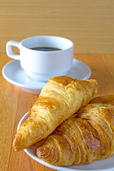 Croissant and a cup of coffee on wood table