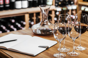 close-up shot of decanter of red wine with notebook and glasses on wooden table at wine storage