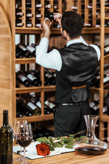 red wine and red rose on table at wine store with blurred wine steward on background
