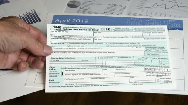 Hand picking up Form 1040 Simplified allows filing of taxes on postcard