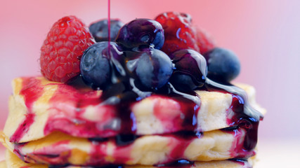 Stack of pancakes with raspberries, blueberries and drizzled with blueberry maple syrup, macro closeup.