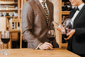 cropped shot of female wine steward wine for customer from decanter at wine store