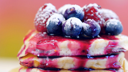 Stack of pancakes with raspberries, blueberries and drizzled with blueberry maple syrup, macro closeup.