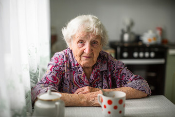 An elderly russian woman sitting at the kitchen table. - obrazy, fototapety, plakaty