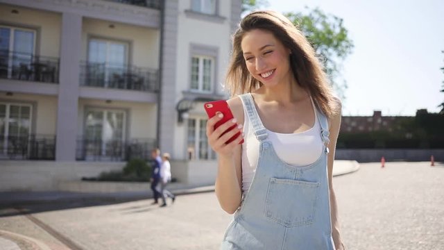 Gorgeous young woman in trendy outfit walks and texts messages via her smarpthone. Social networks, instagram, fashion blogger. Modern technologies, devices. Female portrait
