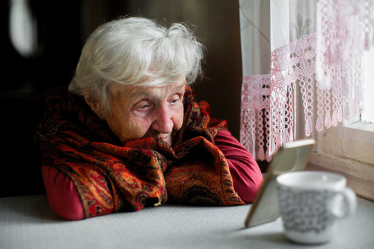 An elderly woman sitting at the table looking at the screen of the smartphone.