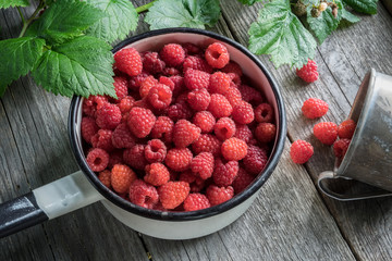 Bowl full of raspberries and rustic mug with ripe scattered berries.