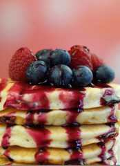 Stack of pancakes with raspberries, blueberries and drizzled with blueberry maple syrup, macro closeup.