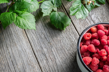 Bowl full of raspberry berries and leaves on wooden board. Top view. Copy space for text.