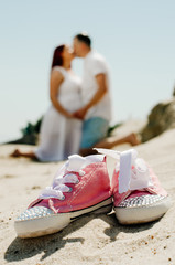 Naklejka premium photo shoot of a pregnant couple on the beach. the girl has red hair . small sneakers pink