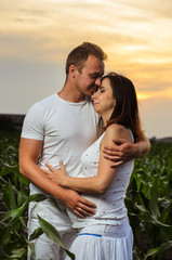 pregnant woman , expectant mother . dressed in white, family photo shoot at sunset in a field . husband listening to pregnant belly