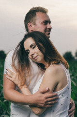 pregnant woman , expectant mother . dressed in white, family photo shoot at sunset in a field . husband listening to pregnant belly