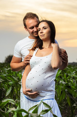 pregnant woman , expectant mother . dressed in white, family photo shoot at sunset in a field . husband listening to pregnant belly