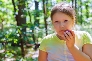 Child girl eating an red apple in a park in nature.