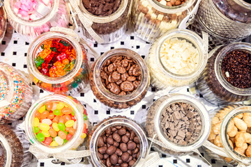 Top view glass containers with various additives to ice cream. Choice of filler - candies, nuts, jelly sweets, chocolate, coconut, marshmallow. onfectionery display. Selective focus. Close up.