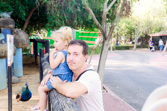 Portrait of father holding his toddler daughter looking to the nature in the zoo park. Family rest, spending time together concept. Selective focus. Copy space.