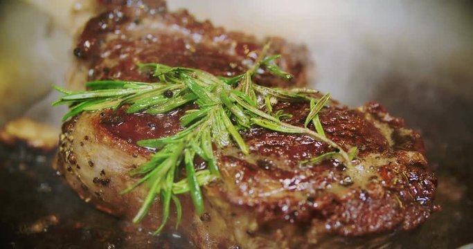 Juicy beef steak with fresh rosemary is frying on a pan in a modern restaurant