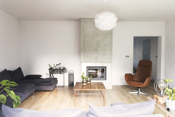Modern and beautiful home interior with design sofa, wooden table and fireplace. Bright and sunny living room with plants and brown wooden floor.