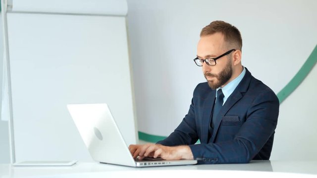 Attractive businessman in suit and glasses working with laptop in white office