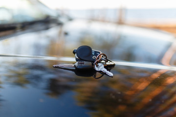 Keys with immobilizer on the hood of the car against the window. Beautiful summer light and sun. The hood reflects the sunset and the sun's rays with the scenery of nature